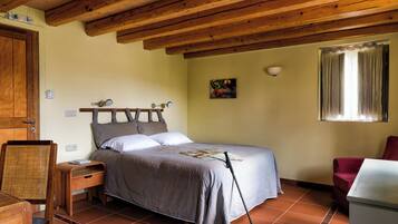 A bedroom with a wooden ceiling, a bed with a headboard, a nightstand, a chair, a table, and a window with curtains.