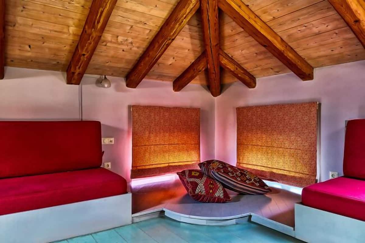 Une pièce chaleureuse avec un plafond en pente, des poutres en bois et des sièges recouverts d’un tissu rouge.