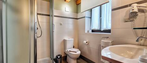 Un baño con ducha envuelta en cristal, inodoro, lavabo y ventana con cortinas.