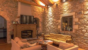 Una habitación con paredes de piedra, chimenea, televisor y sofá.
