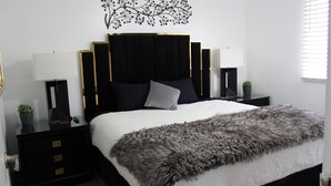 Een moderne slaapkamer met een groot bed, een zwart hoofdbord, twee nachtkastjes met lampen en een decoratief wandobject.