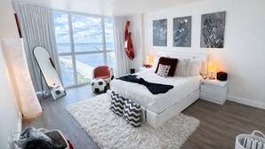 A modern bedroom with a large bed, a view of the sea, and a red chair. - Have a Relaxing getaway from day by day stress
Cozy apartment with stunning view (Fort Myers)