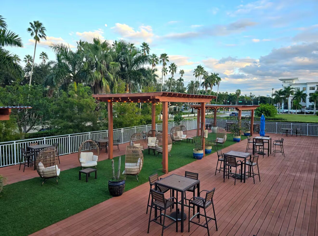 Eine Holzterrasse mit Sitzgelegenheiten im Freien, umgeben von Palmen und einem weißen Zaun.