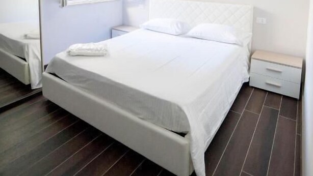 Quarto com cama, mesa de cabeceira, espelho e janela com persianas.