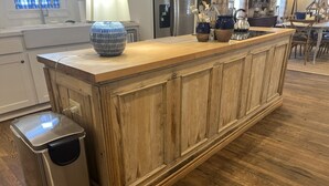 Una cucina con isola in legno, cestino in acciaio inossidabile e finestra con tende azzurre.