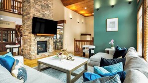 Ein geräumiges Wohnzimmer mit Kamin, einem an einer Steinwand befestigten Fernseher und einer gemütlichen Sitzecke mit Sofa und Sesseln.