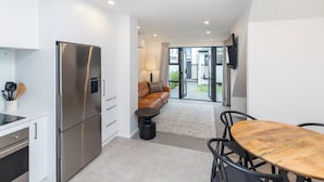 Una cocina moderna con un refrigerador de acero inoxidable, un comedor con una mesa y sillas de madera, y una sala de estar con sofá y televisor.