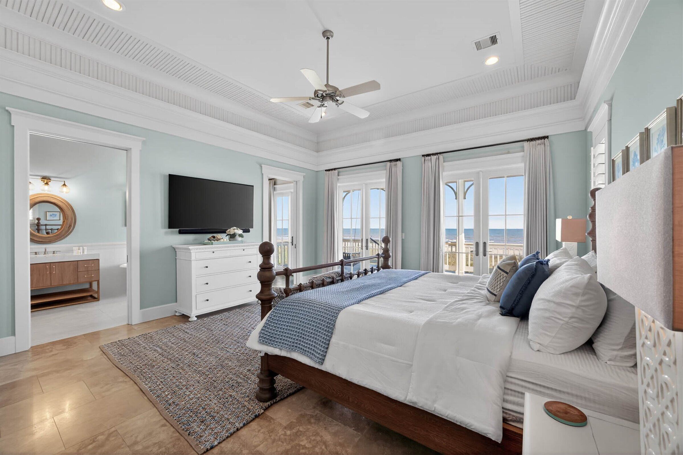 Ein Schlafzimmer mit Bett, Deckenventilator, Fernseher, Kommode und Blick ins Freie.