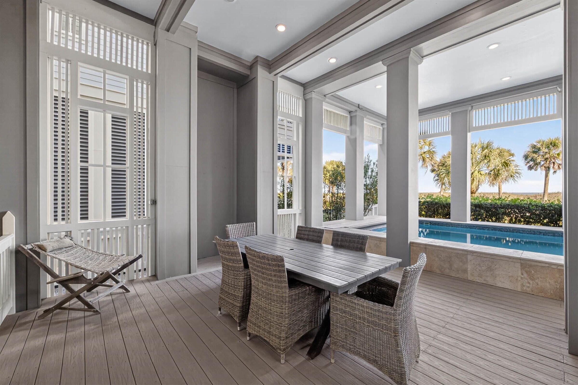 Une terrasse couverte avec une piscine, des meubles en osier et une vue sur les palmiers.