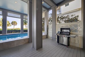An outdoor pool area with a grill and a view of palm trees. - New Beachfront Listing - Heated Pool, Golf Cart, Elevator, Steps to Best Beach (Galveston)
