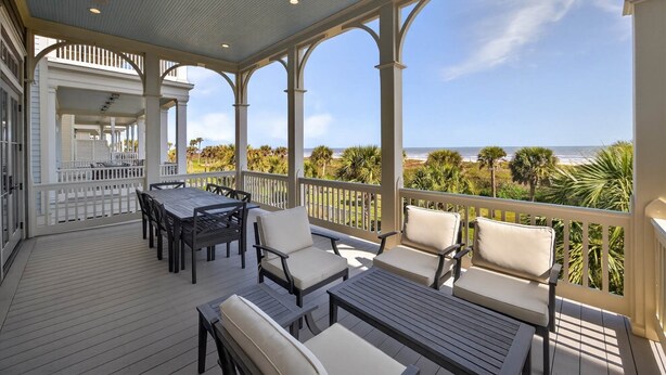 A covered outdoor deck with a table and chairs, overlooking a beach with palm trees. - New Beachfront Listing - Heated Pool, Golf Cart, Elevator, Steps to Best Beach (Galveston)