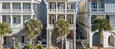 Una hilera de edificios de estilo colonial con balcones, una escalera central y palmeras.