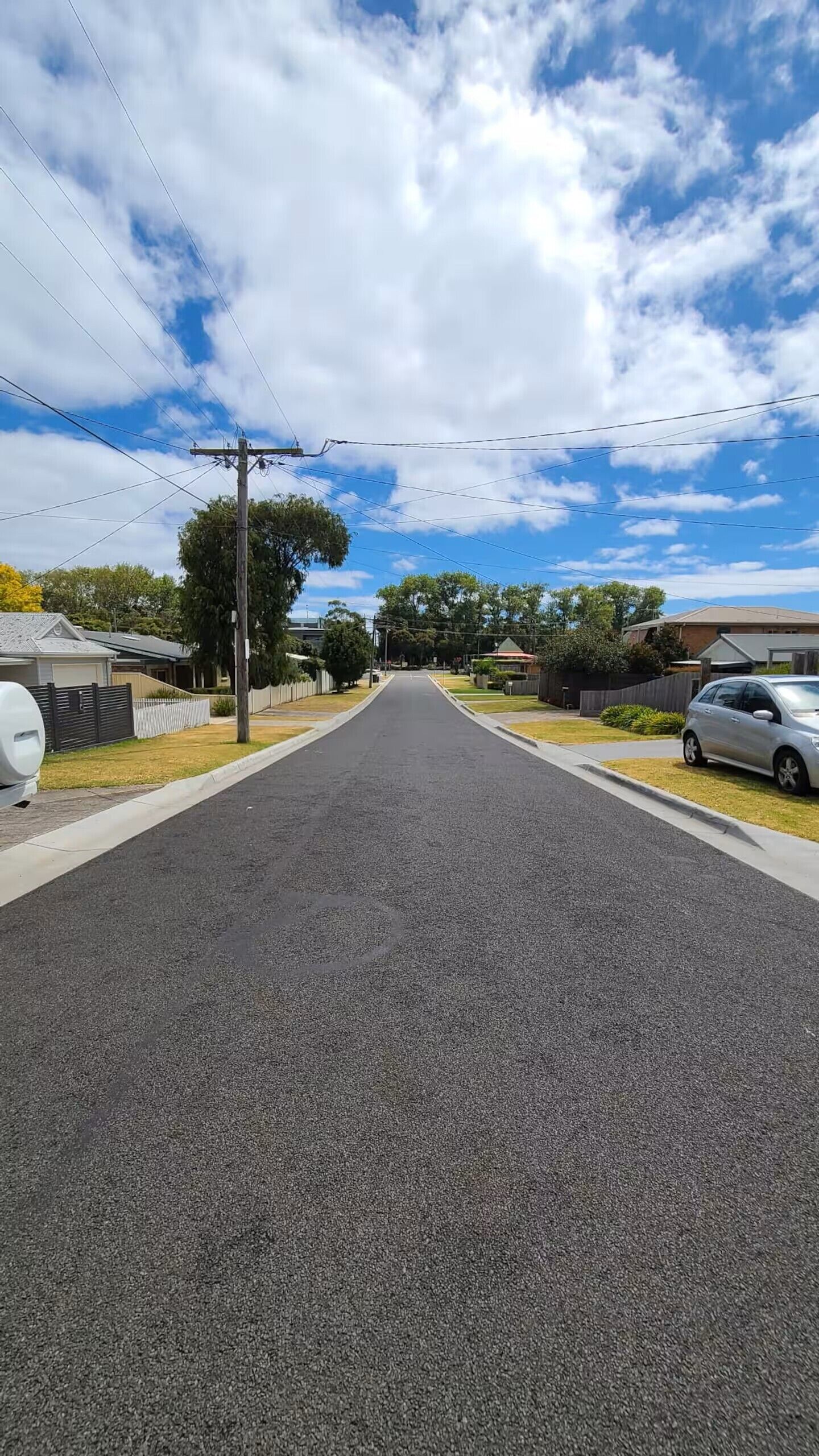 A residential street with houses on both sides, a clear sky, and power lines overhead.