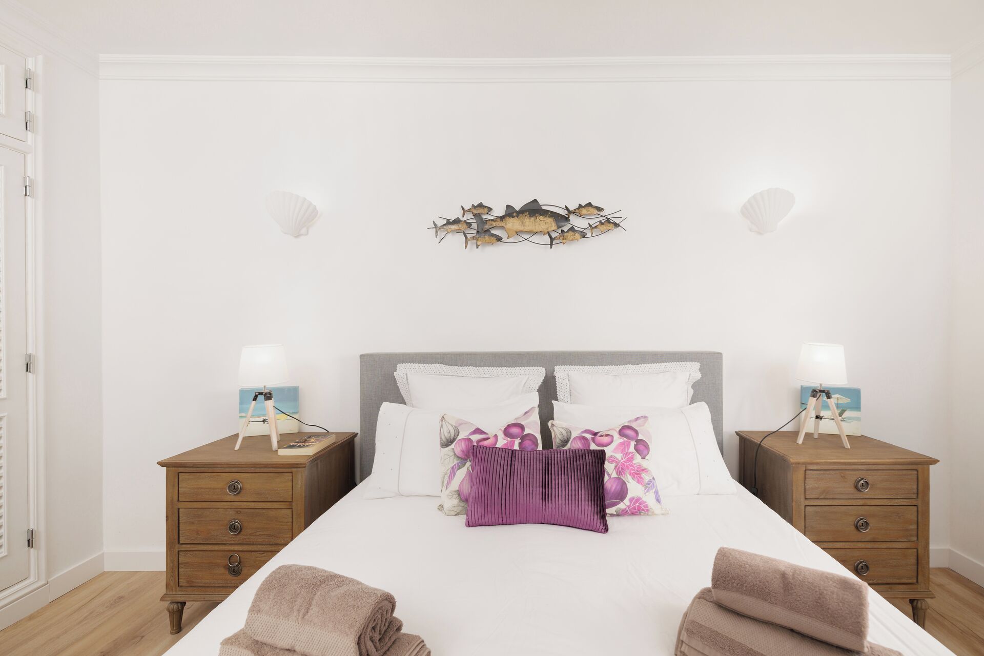 A bedroom with a bed, two bedside tables, a wall decoration, and a nightstand with a lamp.