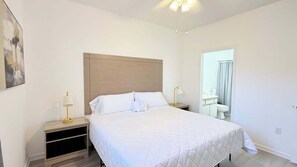A bedroom with a bed, bedside tables, a nightstand, a mirror, and a bathroom door. - Peaceful Golf Course Retreat,2BR First-Floor Condo (Myrtle Beach)