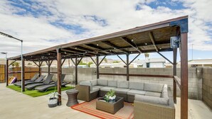Katettu ulkotila, jossa on pergola, pehmustetut istuimet ja pieni pöytä, jonka päällä on ruukkukasveja.