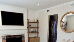 A living room with a beige sofa, a fireplace, a TV, and a kitchen area with a refrigerator. - Old Village Townhome: Dog Friendly, Fireplace, Pool (Mount Pleasant)