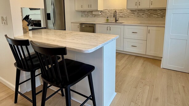 A modern kitchen with white cabinets, a marble island, black bar stools, and pendant lighting. - Old Village Townhome: Dog Friendly, Fireplace, Pool (Mount Pleasant)