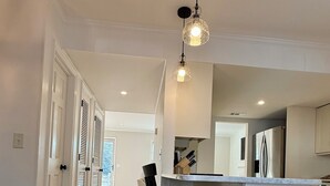 A modern kitchen with a central island, black bar stools, and pendant lighting. - Old Village Townhome: Dog Friendly, Fireplace, Pool (Mount Pleasant)