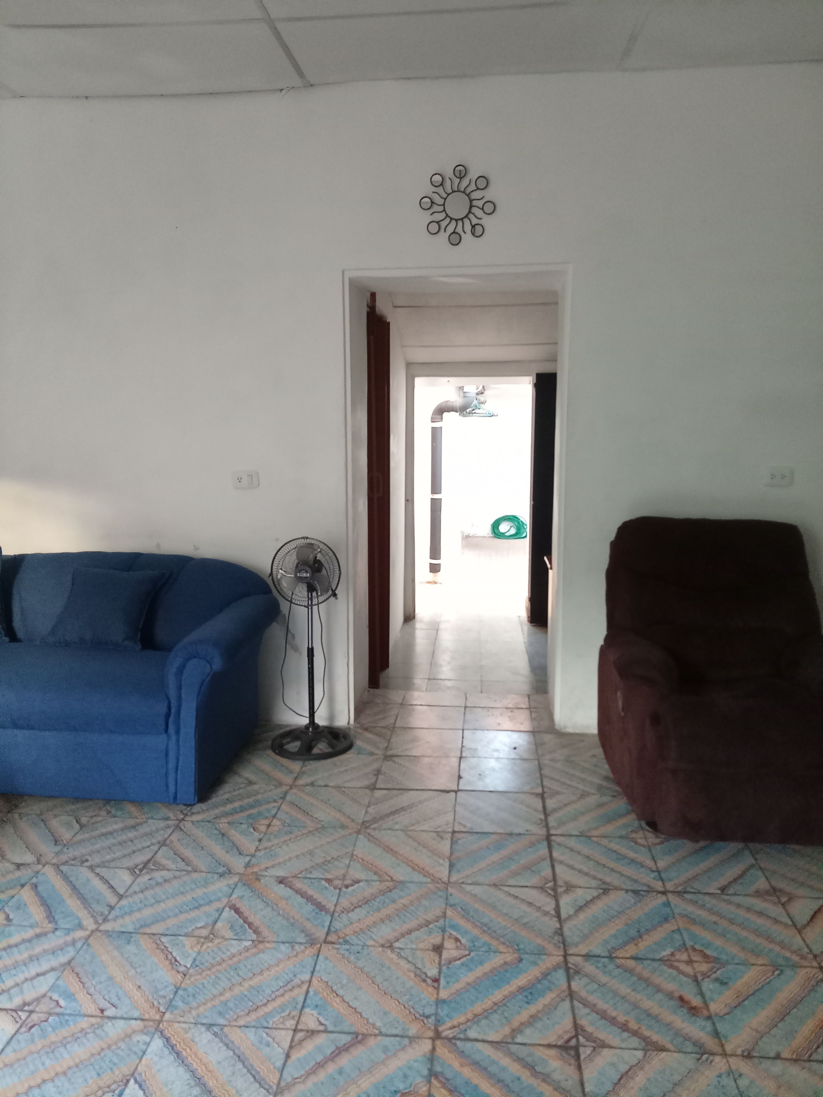 Una sala de estar con piso estampado, un sofá azul, un sillón marrón, un ventilador de pie y un adorno de pared.