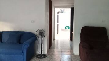 Una sala de estar con piso estampado, un sofá azul, un sillón marrón, un ventilador de pie y un adorno de pared.