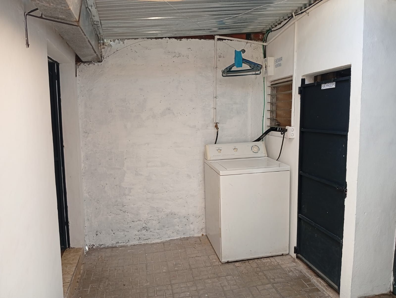 Un lavadero con lavadora, tendedero y una puerta con la inscripción 'BATHROOM'.