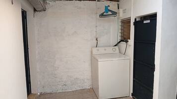 Un lavadero con lavadora, tendedero y una puerta con la inscripción 'BATHROOM'.