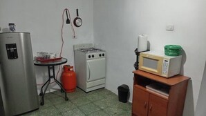 Una cucina compatta con frigorifero, fornello a gas, microonde e un piccolo tavolo con bombola a gas.