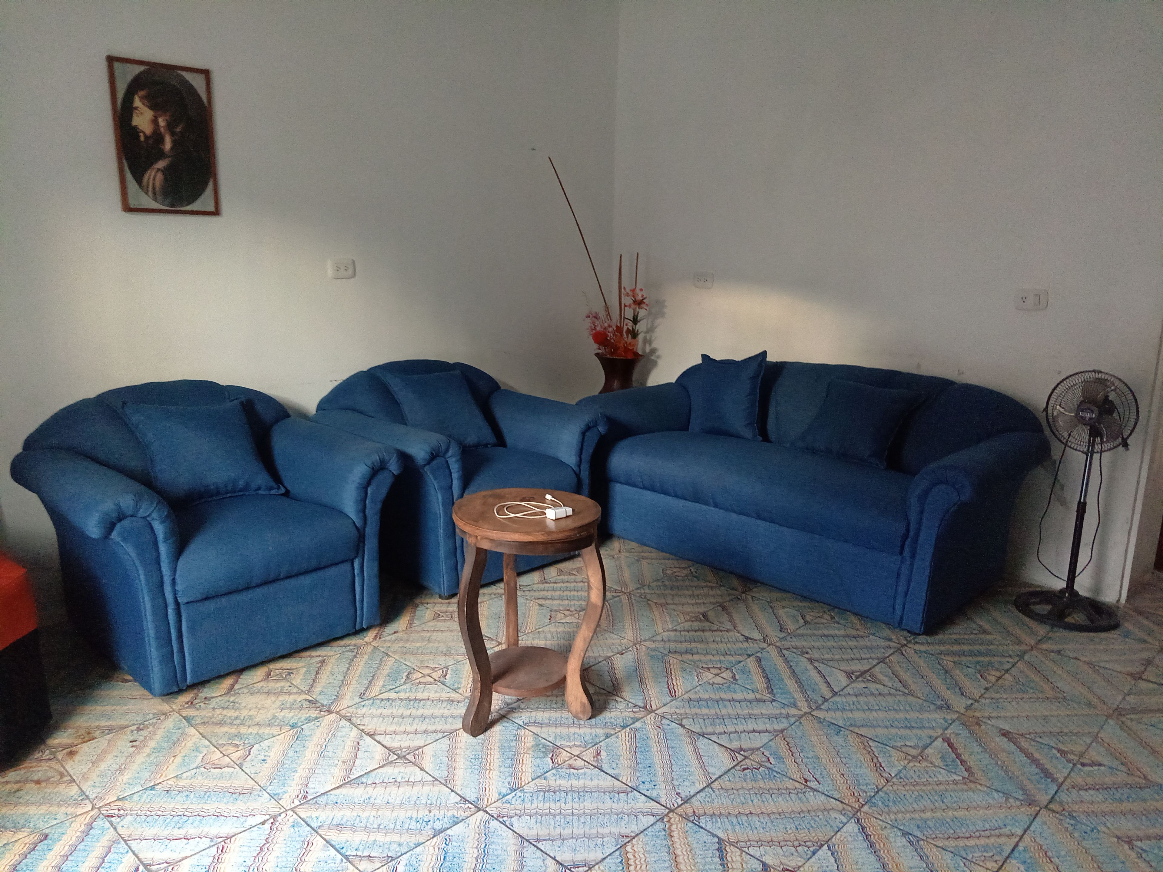 Una sala de estar con un sofá seccional azul, una pequeña mesita de madera, una lámpara de pie y un piso con diseño.