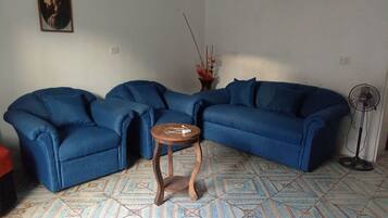 Una sala de estar con un sofá seccional azul, una pequeña mesita de madera, una lámpara de pie y un piso con diseño.
