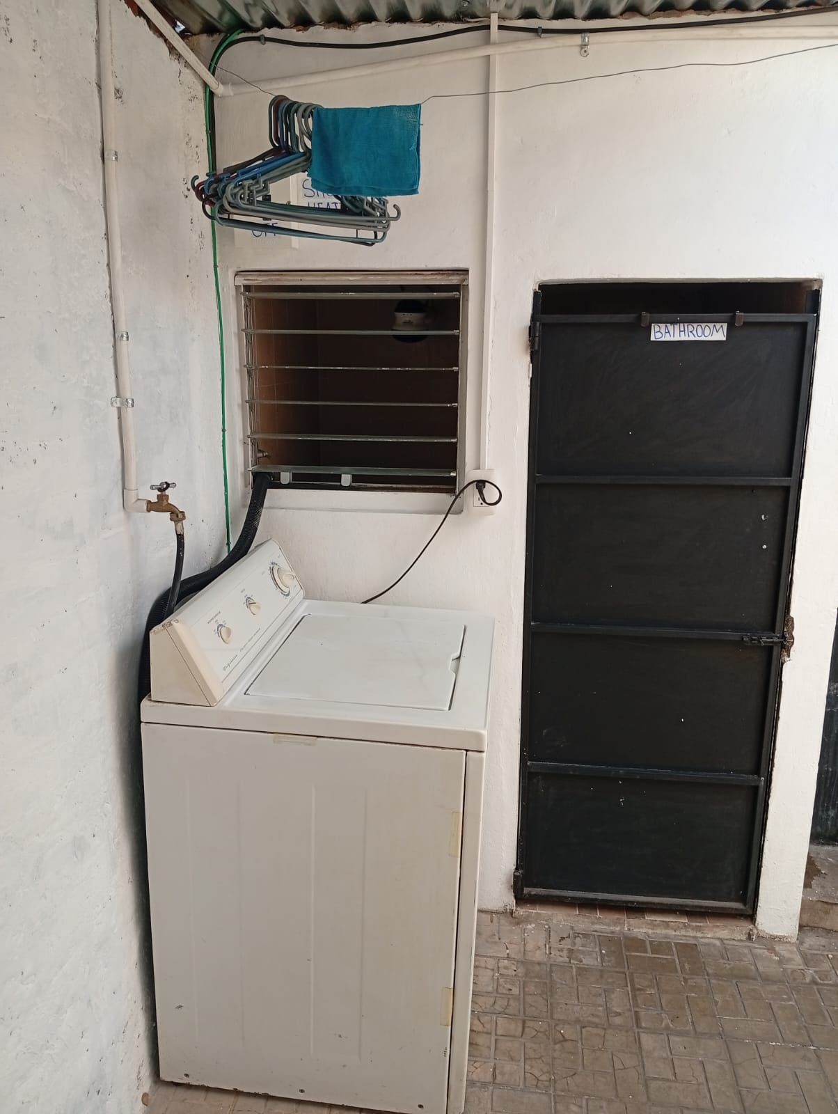 A laundry area with a washing machine, a drying rack, and a black door labeled 'BATHROOM'.
