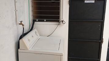 A laundry area with a washing machine, a drying rack, and a black door labeled 'BATHROOM'.