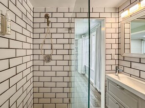 Une salle de bain avec des murs recouverts de carreaux de céramique blancs rectangulaires, une porte de douche en verre, un miroir et un lavabo avec un robinet chromé.