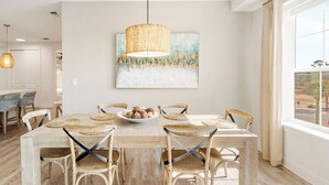 A dining area with a wooden table, woven placemats, and woven chairs. A bowl of bread is on the table, and a painting hangs above. - Sea La Vie Corner Condo at Gulf Place Wraparound Balcony & Beach Access (Santa Rosa Beach)