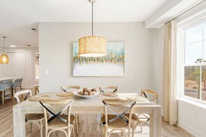 A dining area with a wooden table, woven placemats, and woven chairs. A bowl of bread is on the table, and a painting hangs above. - Sea La Vie Corner Condo at Gulf Place Wraparound Balcony & Beach Access (Santa Rosa Beach)