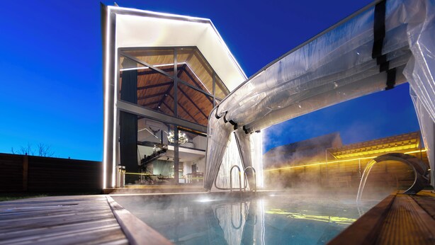 Een modern gebouw met een glazen gevel, een houten terras en een zone met een jacuzzi.