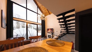 Een moderne eetruimte met een houten tafel, geweven placemats en een groot raam met uitzicht op met sneeuw bedekte bomen.