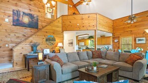 A spacious living room with a large sectional sofa, a wooden staircase, and a kitchen visible through an open doorway. - Breathtaking Views for Family & Friends to Gather (Clarkesville)