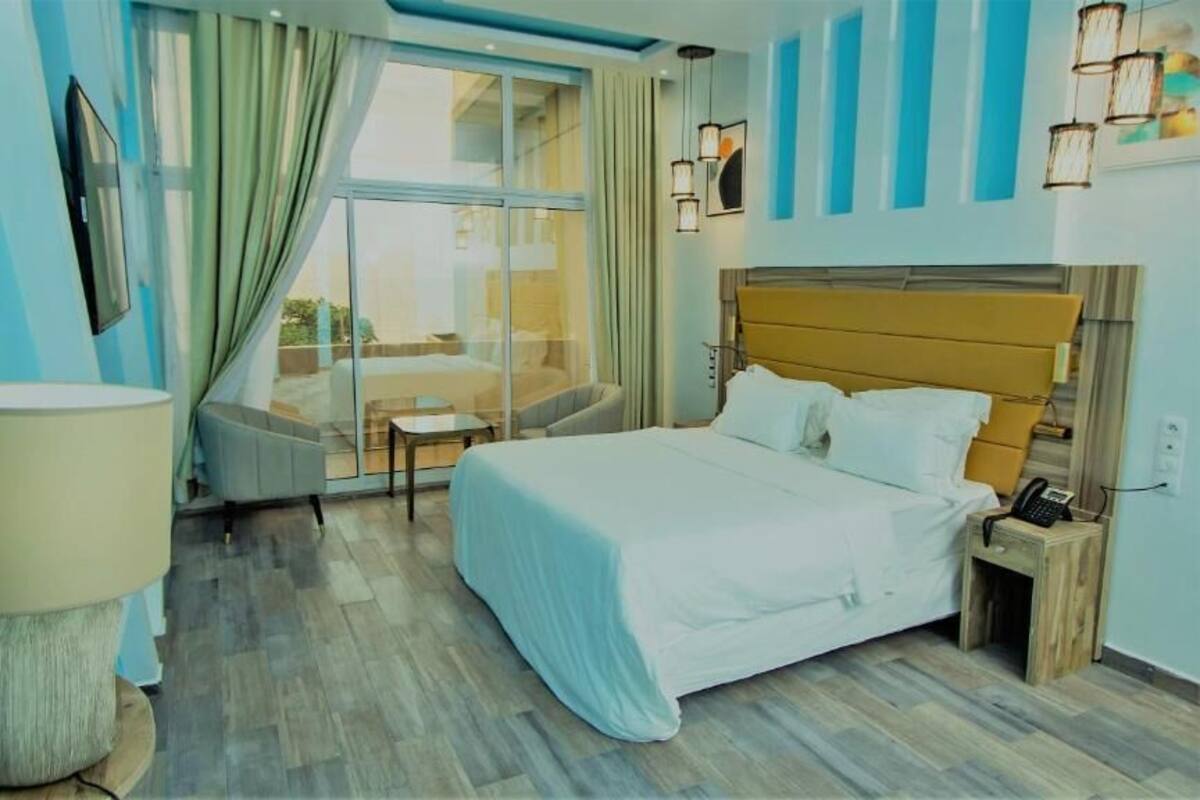 Une chambre d’hôtel avec un grand lit, une table de chevet, une lampe et une vue sur l’extérieur grâce à une grande fenêtre.