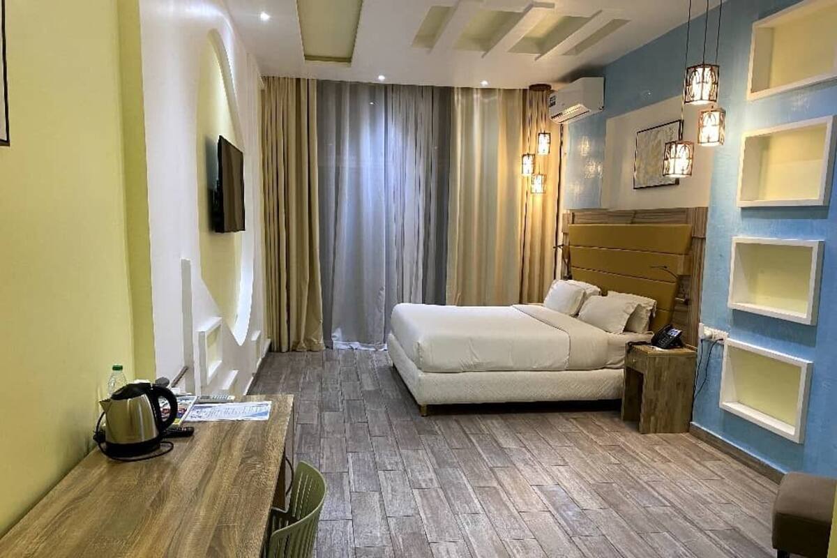 Une chambre d’hôtel avec un lit, un bureau en bois, une chaise, une petite table et un téléviseur fixé au mur.