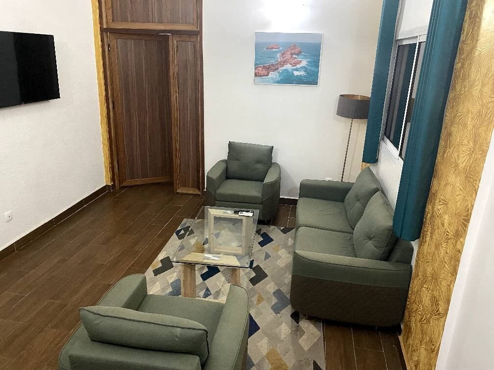 A living room with a sofa, two armchairs, a coffee table, and a TV mounted on the wall.