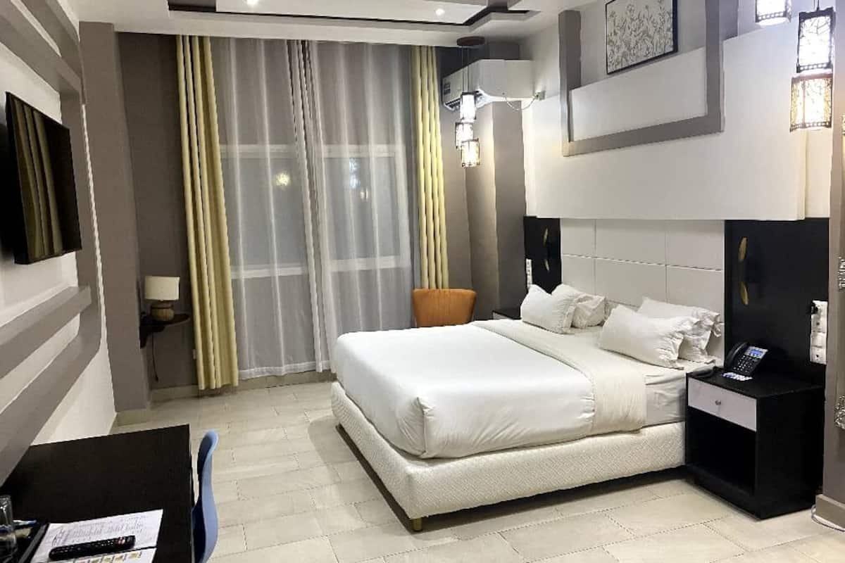 Une chambre d’hôtel moderne dotée d’un grand lit, d’un bureau avec une chaise, d’une table de chevet et d’une grande fenêtre avec des rideaux.