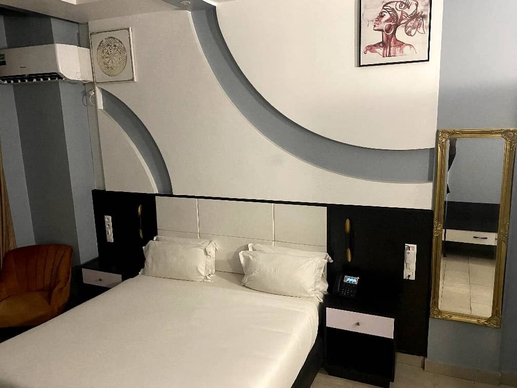 A hotel room with a bed, bedside tables, a chair, a mirror, and a wall-mounted artwork.