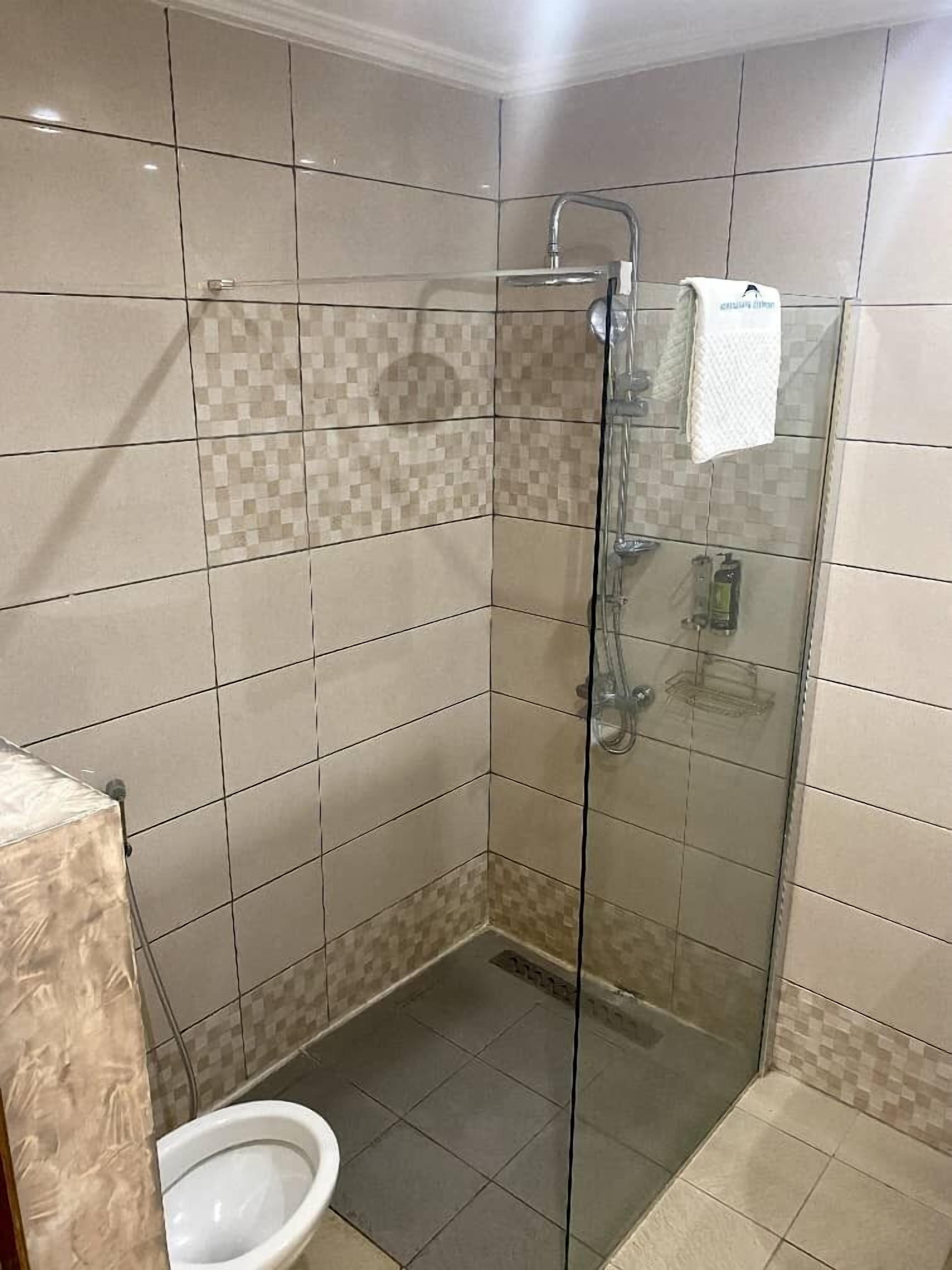 A glass-enclosed shower stall with a handheld showerhead, a glass door, and a tiled floor.