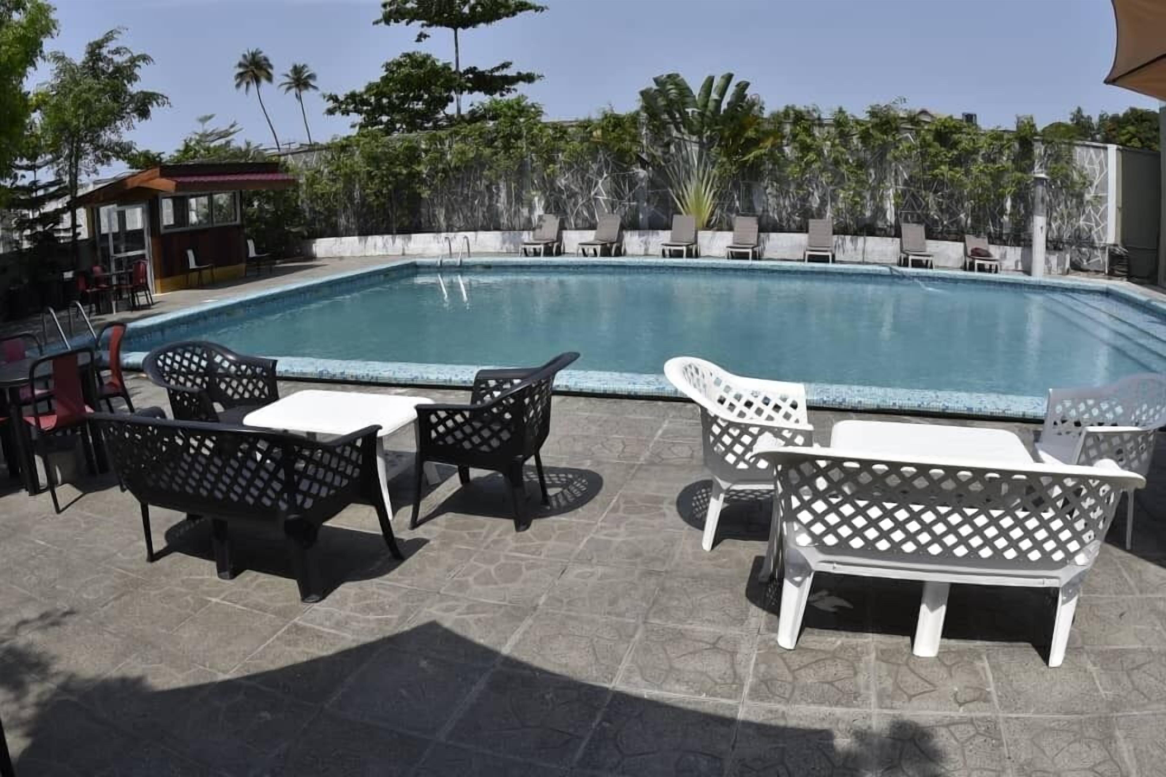 Un área de piscina con sillas de descanso y mesas, rodeada por un patio de piedra y vegetación.