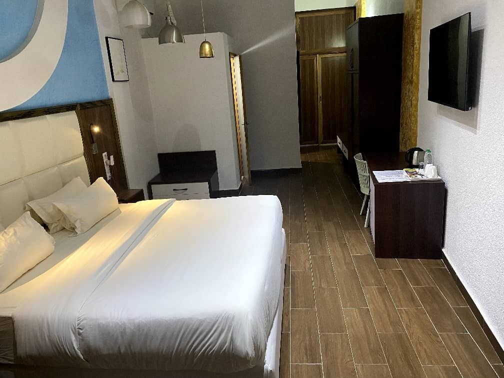 A hotel room with a large bed, a desk, a chair, a TV, and a wardrobe.