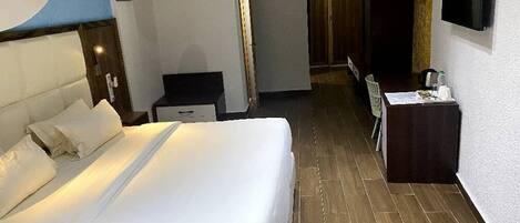 A hotel room with a large bed, a desk, a chair, a TV, and a wardrobe.