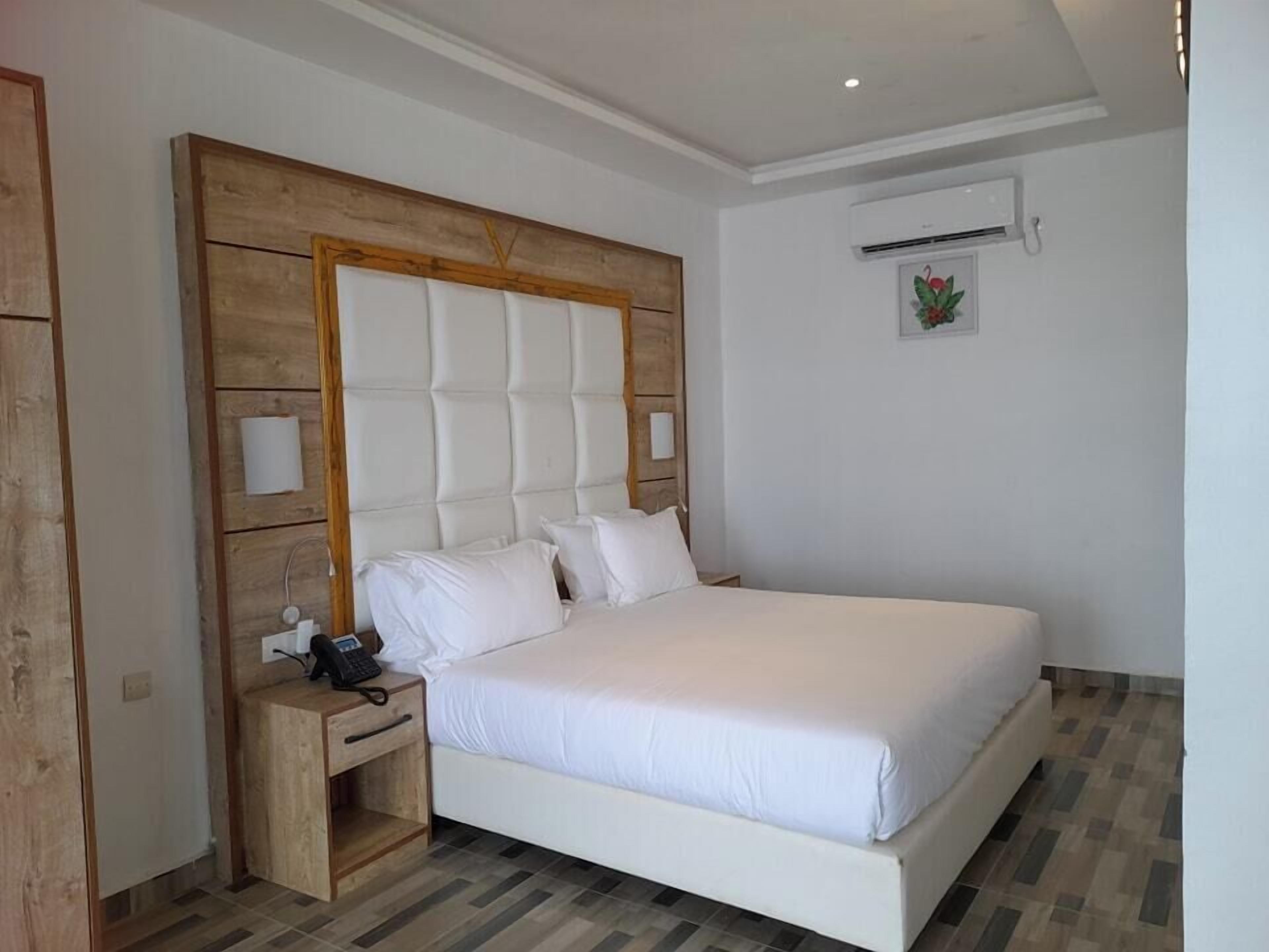 Un dormitorio con una cama grande, un cabecero de madera, una mesita de noche con un teléfono y un equipo de aire acondicionado pequeño montado en la pared.