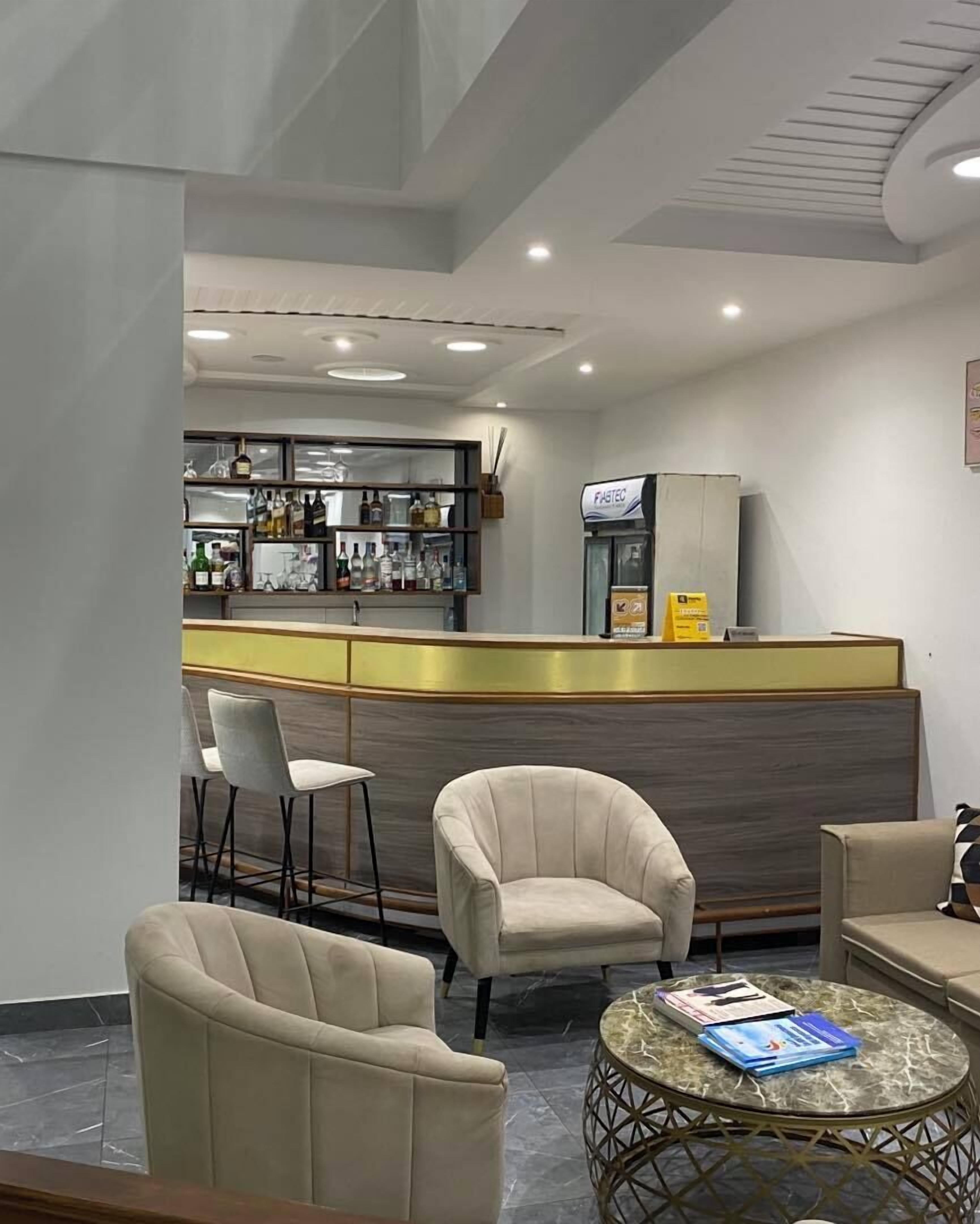 Un espace bar moderne comprenant un comptoir, des tabourets de bar et un coin salon avec des fauteuils et une table ronde.