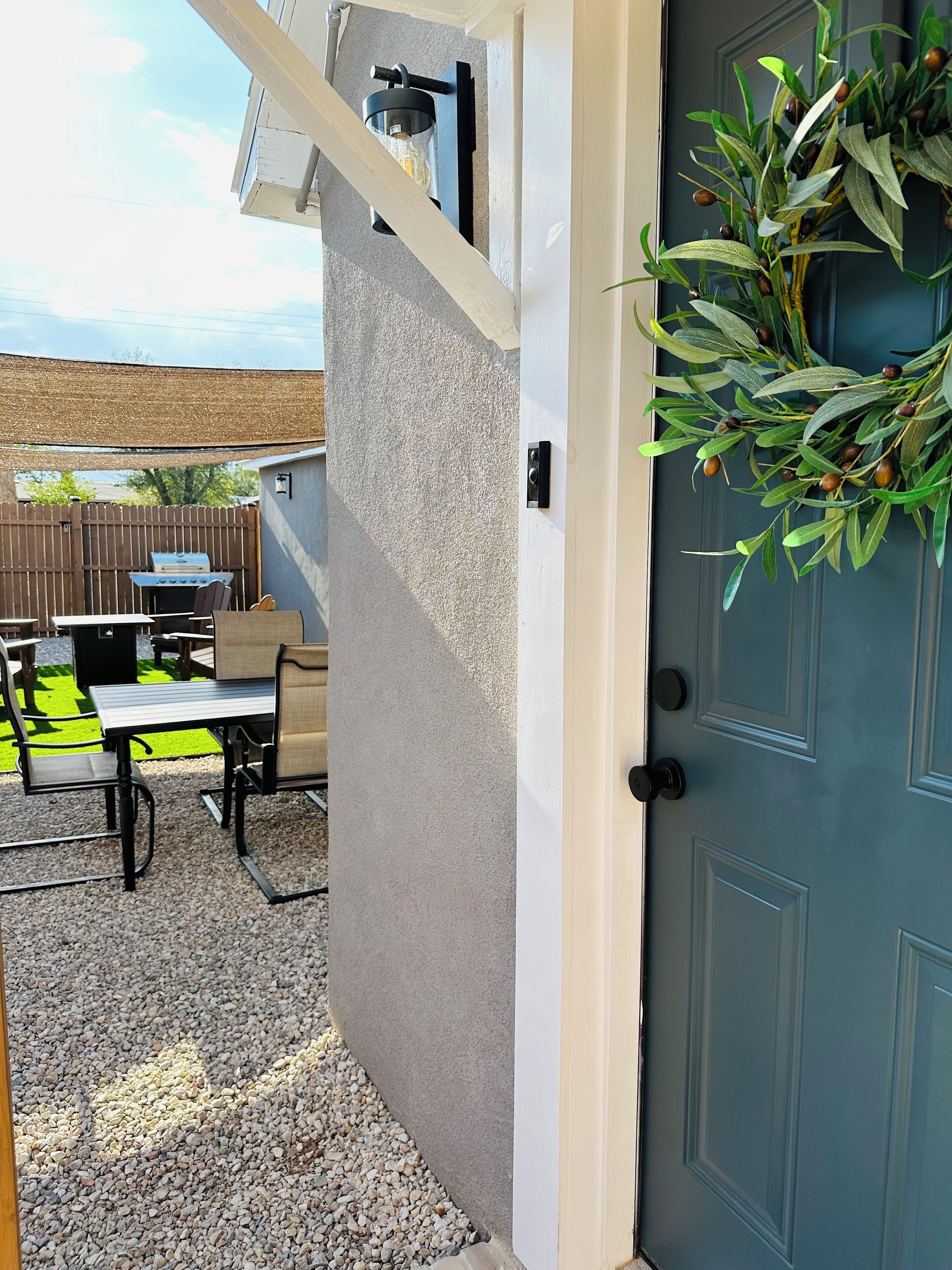 Un patio con una parrilla, mobiliario exterior y una planta decorativa cerca de una puerta.